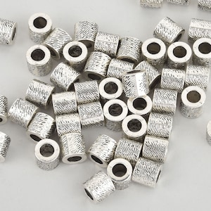 May include: A pile of silver metal beads with a textured surface. The beads are round with a hole in the center.