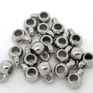 May include: A pile of silver-toned metal bead caps with a small loop on the top. The bead caps are round and have a smooth finish.
