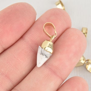 May include: A white and gold pendant with a pointed tip. The pendant is made of a white stone with a gold cap on top. The pendant has a gold loop at the top for attaching to a chain.