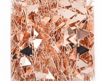 May include: Close-up of a roll of rose gold chain with triangle-shaped charms. The charms are connected by small rings, creating a decorative chain. The chain is tightly wound, showing the reflective surface of the metal.