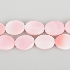 May include: A close-up shot of a strand of light pink, flat, oval-shaped beads. The beads are evenly spaced and have a smooth, polished surface. The background is a solid, light gray color.