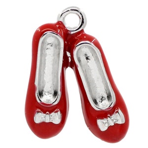 May include: A pair of red enamel charm shoes with silver-colored interiors and bows. The charm has a silver-colored loop at the top for attaching to a bracelet or necklace. The shoes are a glossy red.