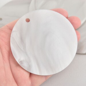 May include: A white, round, marbled, plastic blank with a hole in the center. The blank is smooth and has a subtle swirl pattern.