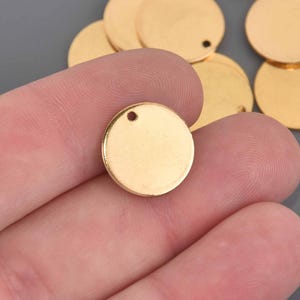 May include: Gold-colored, round metal charms with a small hole at the top for jewelry making or crafting. The charms are smooth and shiny, perfect for creating personalized pendants or earrings. Several charms are visible.