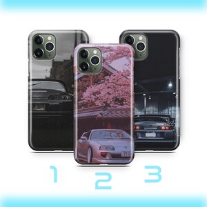 Puede incluir: Tres fundas para teléfono con diseños de coches. La primera funda es en blanco y negro con un coche frente a un edificio. La segunda funda tiene un diseño floral rosa con un coche. La tercera funda es negra con un coche.