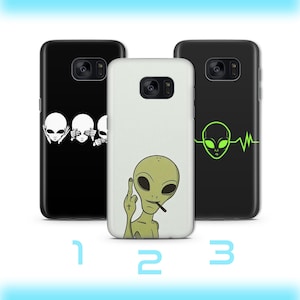 Peut inclure: Trois coques de téléphone avec des motifs d'extraterrestres. L'une est noire avec trois visages d'extraterrestres, une autre est blanche avec un extraterrestre faisant un doigt d'honneur, et la troisième est noire avec une tête d'extraterrestre verte et une ligne de battement de cœur.