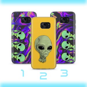 May include: Three phone cases. The case in the center is yellow with a gray alien head graphic. The other two cases have a swirling purple and green background with green alien graphics. The cases are numbered 1, 2, and 3.