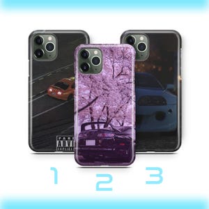 Op de afbeelding: Drie telefoonhoesjes met auto-ontwerpen. Eén hoesje toont een kleine oranje auto op een weg, een ander een zwarte auto onder roze kersenbloesems en de derde een blauwe auto.