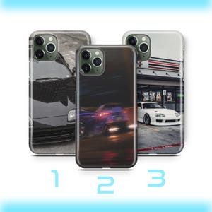 Peut inclure: Trois coques de téléphone avec des designs de voitures. La première coque présente une voiture noire sur fond gris. La deuxième coque a une image floue d'une voiture avec des lumières rouges et bleues. La troisième coque montre une voiture blanche garée devant un magasin.