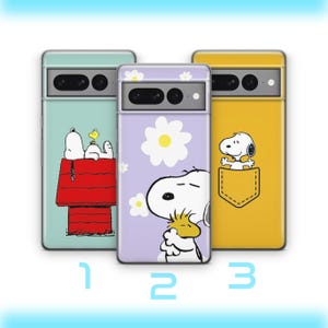 May include: Three phone cases with cartoon character designs. The first case is light blue with Snoopy and Woodstock on a red doghouse. The second case is lavender with Snoopy and a daisy. The third case is yellow with Snoopy in a pocket.