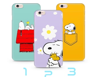 Puede incluir: Tres fundas de teléfono coloridas con diseños de Snoopy y Woodstock. Una funda es azul claro con Snoopy en su caseta, otra es lavanda con una margarita y la tercera es amarilla con Snoopy en un bolsillo.