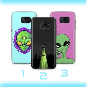 Könnte beinhalten: Drei Handyhüllen mit Alien-Motiven. Eine Hülle ist hellblau mit einem grünen Alienkopf in einem lila Portal. Eine andere ist schwarz mit einem UFO und einem grünen Strahl. Die dritte ist rosa mit einem grünen Alien.