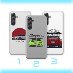 May include: Three smartphone cases featuring Toyota Supra car graphics. The left case is white with a red circle and silver car. The centre case is grey with a green car and the text Supra. The right case is white with a red car and engine art.