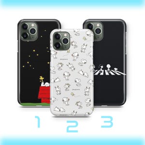Könnte beinhalten: Drei Handyhüllen mit Snoopy-Designs. Eine Hülle ist schwarz mit Snoopy auf seinem Hundehütte unter einem Sternenhimmel. Eine andere ist weiß mit Snoopy in verschiedenen Posen. Die dritte ist schwarz mit Snoopy, der eine Straße überquert.