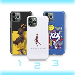 May include: Three phone cases with basketball designs. One case features a player in a yellow jersey with a crown, another shows a player mid-jump with the text "I am the king of this game!", and the third has a cartoon character.