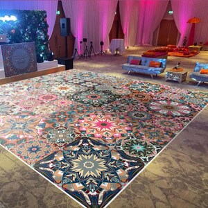 May include: A large, patterned floor covering with a geometric design. The floor covering features a variety of colours, including pink, blue, orange, and green. The floor covering is in a large room with couches and tables.
