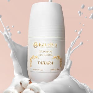 Peut inclure: Bouteille de déodorant roll-on blanche avec des détails dorés, le texte "TAHARA" est visible. La bouteille est entourée d'une éclaboussure de liquide blanc et de fleurs de coton. Le produit est de 50 ml.