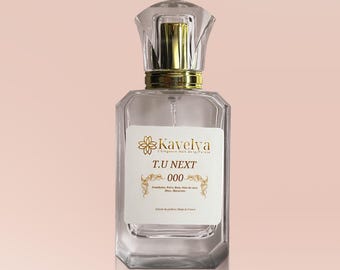 May include: A clear glass perfume bottle with a gold-colored neck and a faceted cap. The white rectangular label features the gold text Kavelya, T.U NEXT, 000, and smaller printed details including Framboisier, Poire, Rose, Bois de coco, Musc, Macarons.