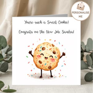 May include: A square greeting card with a white background featuring a cartoon chocolate chip cookie with a smiling face, pink cheeks, and raised arms. The text reads: You're such a Smart Cookie! Congrats on the New Job, Sandra! Colourful sprinkles surround the cookie.