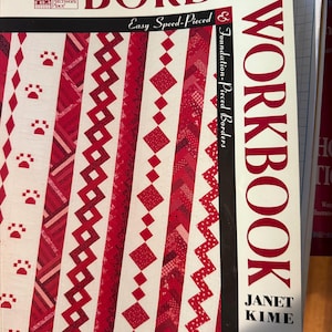 May include: A softcover book titled The Border Workbook by Janet Kime. The cover features a white background with red text and a vertical display of various red and white quilt border patterns, including paw prints, diamonds, and zigzags.