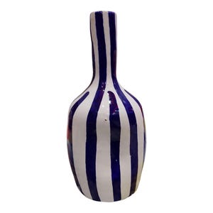 May include: A tall, ceramic vase with a rounded base and a long, narrow neck. The vase is painted with vertical stripes of white and deep blue. The stripes are uneven, giving the vase a handmade appearance. The vase is suitable for home decor.