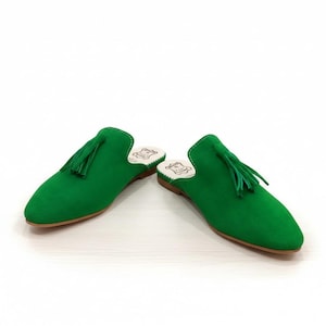 May include: A pair of bright green suede slip-on shoes with pointed toes and a small tassel on the top. The shoes have a low heel and a light-colored interior.
