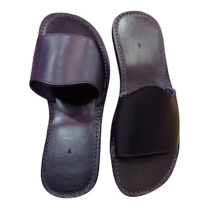 May include: A pair of black leather slide sandals. The sandals have a simple design with a single strap across the top of the foot. The soles are stitched and the sandals are size 4.