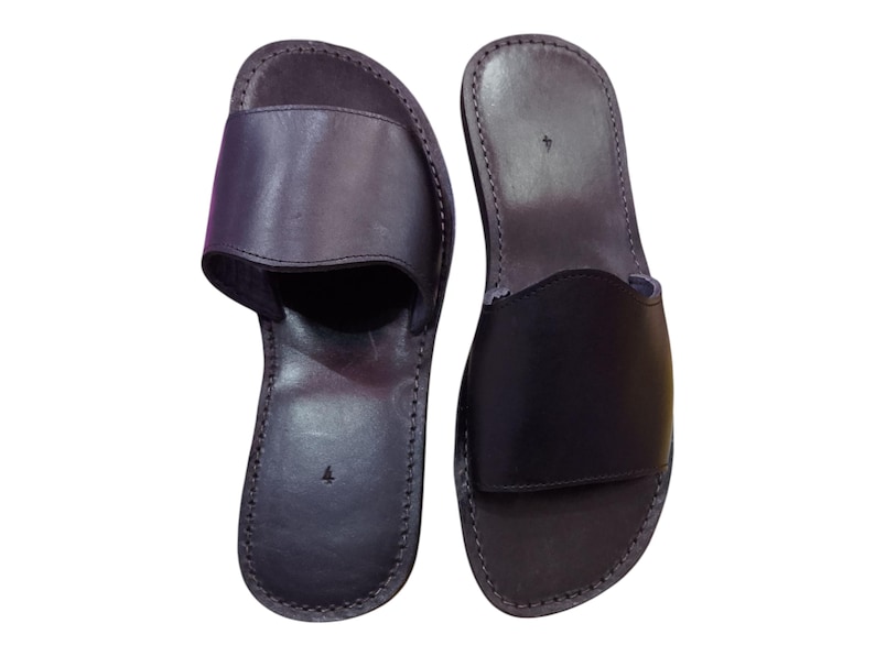 May include: A pair of black leather slide sandals. The sandals have a simple design with a single strap across the top of the foot. The soles are stitched and the sandals are size 4.
