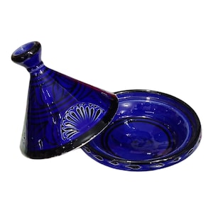 May include: A cobalt blue tagine, a traditional Moroccan cooking pot, with a conical lid and a shallow base. The lid features black and white decorative patterns. The base has a black rim and a similar design.