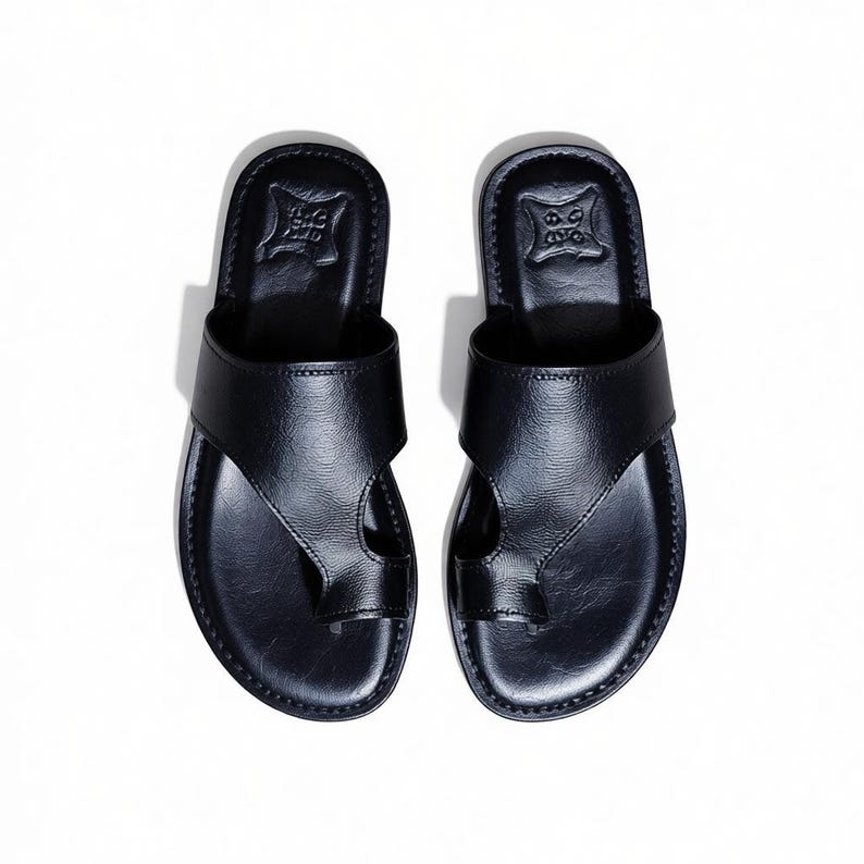 May include: A pair of black leather sandals with a toe loop design. The sandals have a strap across the top of the foot and a textured sole. The sandals are displayed on a white background.