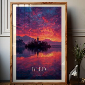 May include: A framed vertical art print featuring a vibrant sunset over Lake Bled in Slovenia. The scene depicts a church on a small island with mountains in the background, reflected in the water. The text BLED and SLOVENIA appears at the bottom.