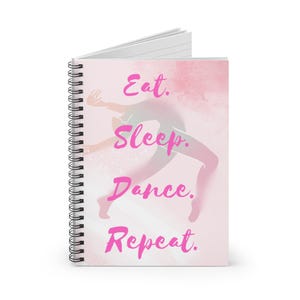 May include: Spiral-bound notebook with a pink cover. The cover has the words "Eat. Sleep. Dance. Repeat." in a cursive font. A dancer silhouette is in the background, with a watercolour-like effect.