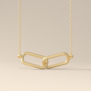 May include: A gold-coloured necklace with a chain and a pendant of two interlocking oval links. The necklace is set against a neutral background. The word "Orielle" is in the bottom right corner.