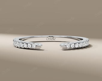 Pode incluir: Um anel prateado com uma fileira de pequenas pedras preciosas transparentes. O anel tem um design aberto, com as extremidades da banda não conectadas. A palavra "Orielle" está gravada no anel. O anel é exibido em um fundo neutro.