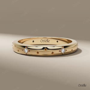 May include: A gold ring with a polished finish. The ring features star-shaped cutouts and is adorned with small diamonds. The word "Orielle" is engraved on the ring. This ring is a piece of jewellery.