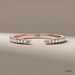 May include: Rose gold ring with a row of small, sparkling diamonds. The ring has an open design, with the brand name "Orielle" engraved on the band. The ring is displayed on a neutral background.