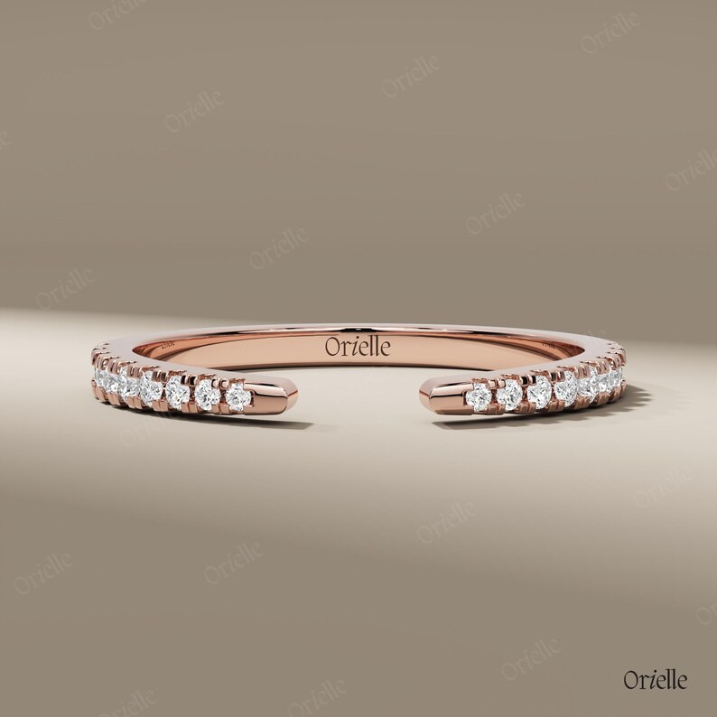 May include: Rose gold ring with a row of small, sparkling diamonds. The ring has an open design, with the brand name "Orielle" engraved on the band. The ring is displayed on a neutral background.