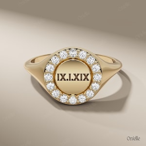 Puede incluir: Un anillo de sello dorado con una cara redonda. La cara está rodeada por un anillo de pequeñas piedras preciosas transparentes. El centro del anillo presenta los números romanos IX.I.XIX. El anillo tiene un acabado pulido y un diseño clásico.