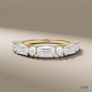May include: A gold ring with a series of alternating emerald and round cut clear gemstones. The ring has the brand name "Orielle" engraved on the band.