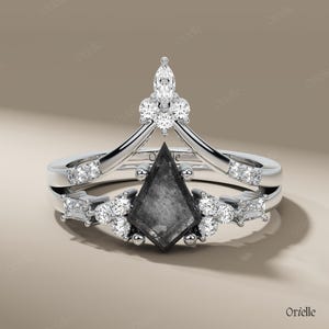 May include: A silver engagement ring set featuring a kite-shaped, dark gray center stone. The ring is accented with multiple round and baguette-cut white gemstones. The design includes a crown-like top and a matching band.