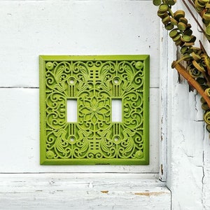 May include: A green metal light switch cover with a decorative floral design.