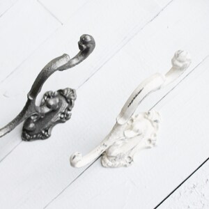 May include: Two decorative wall hooks with ornate designs. One hook is black and the other is white.
