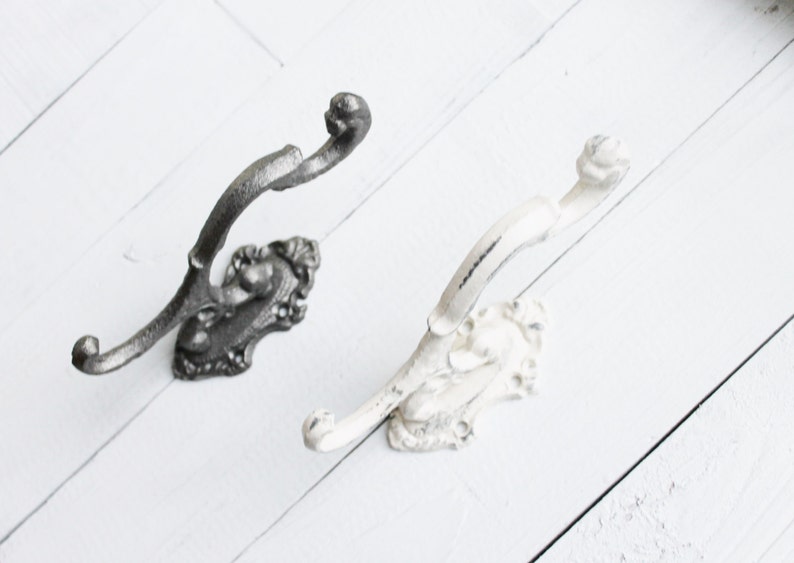 May include: Two decorative wall hooks with ornate designs. One hook is black and the other is white.