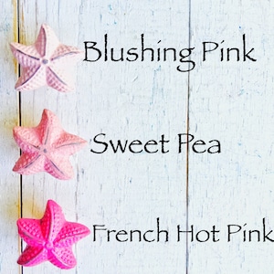 May include: Three pink starfish on a white wooden background. The starfish are labeled "Blushing Pink", "Sweet Pea", and "French Hot Pink".