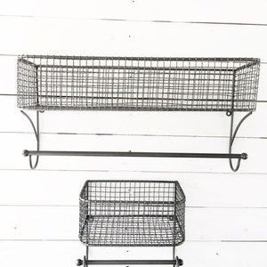 May include: Two black metal wire shelves with towel bars. The top shelf is larger than the bottom shelf. Both shelves have a simple, industrial design.