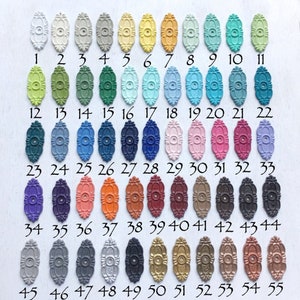 May include: A chart of 55 small oval-shaped metal knobs with different colors and finishes. The knobs are arranged in rows of 11. The numbers 1 through 55 are printed below each knob.