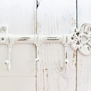 May include: White key-shaped coat rack with three hooks. The rack is made of metal and has a distressed finish.