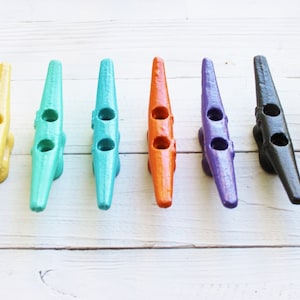 May include: A set of eight colorful boat cleats, each painted a different color: yellow, teal, turquoise, orange, purple, black, silver, and white.