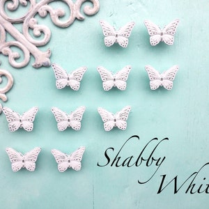 May include: Ten white butterfly-shaped decorative embellishments on a light blue background. The text "Shabby White" is written in black cursive lettering.