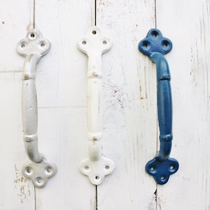 May include: Three cast iron door handles in different colors: white, light blue, and dark blue. Each handle has a decorative, ornate design at the top and bottom.